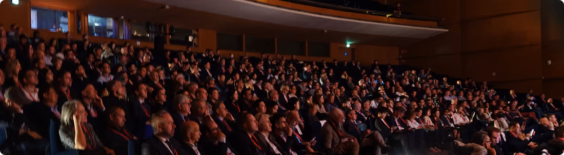 Large audience seated in an auditorium, attentively facing forward.