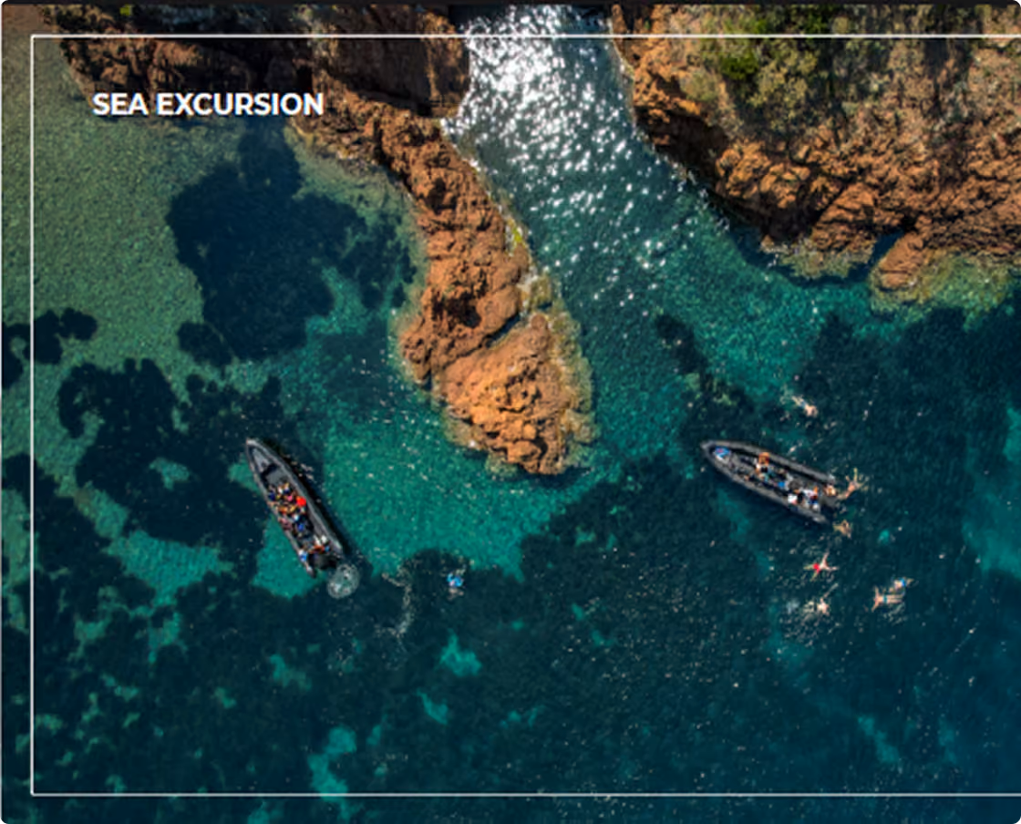 Aerial view of a sea excursion with two boats floating near rocky formations in clear turquoise water, with several people swimming nearby.