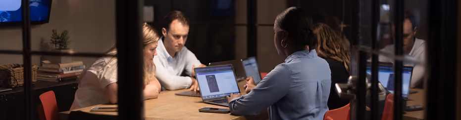 Team working on laptops around a boardroom table in the evening