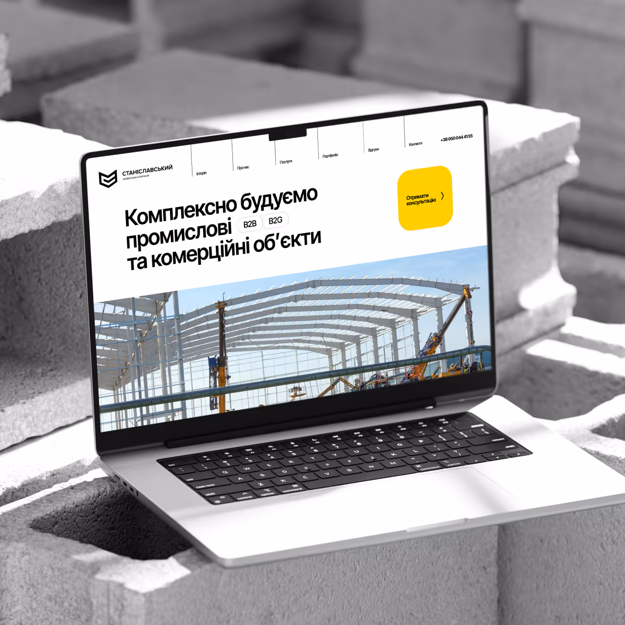 Laptop on concrete blocks shows a construction company site with industrial building framework.