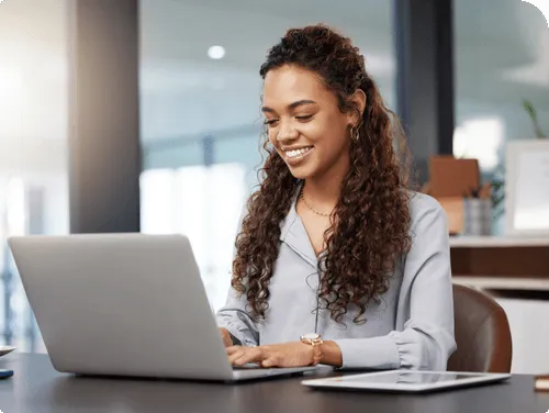 A smiling woman with curly hair sits at a table with a laptop in front of her, ready to drive your business forward. Nearby, another person is typing on a keyboard. An overlay on the image shows an "Inventory" screen featuring images of a red dress and items listed, showcasing leading-edge features.