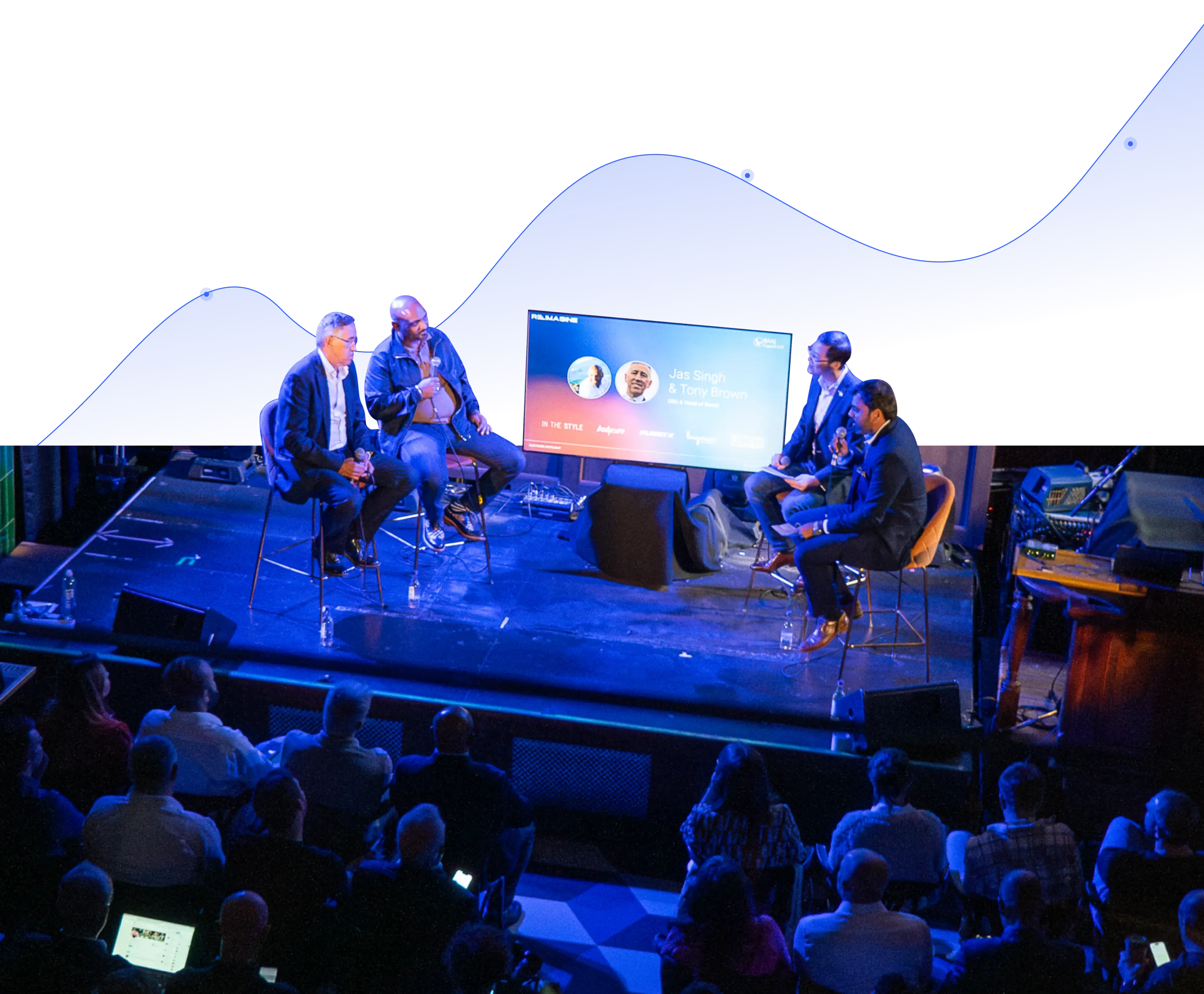 A group of people sitting on stage with a screen in the background.