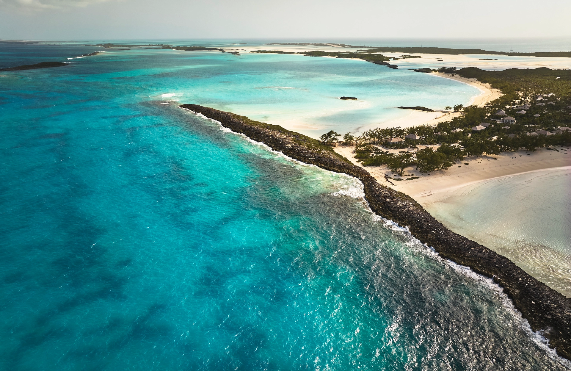 Aerial view of a tropical island with turquoise waters, sandy beaches, and small buildings near the shore.