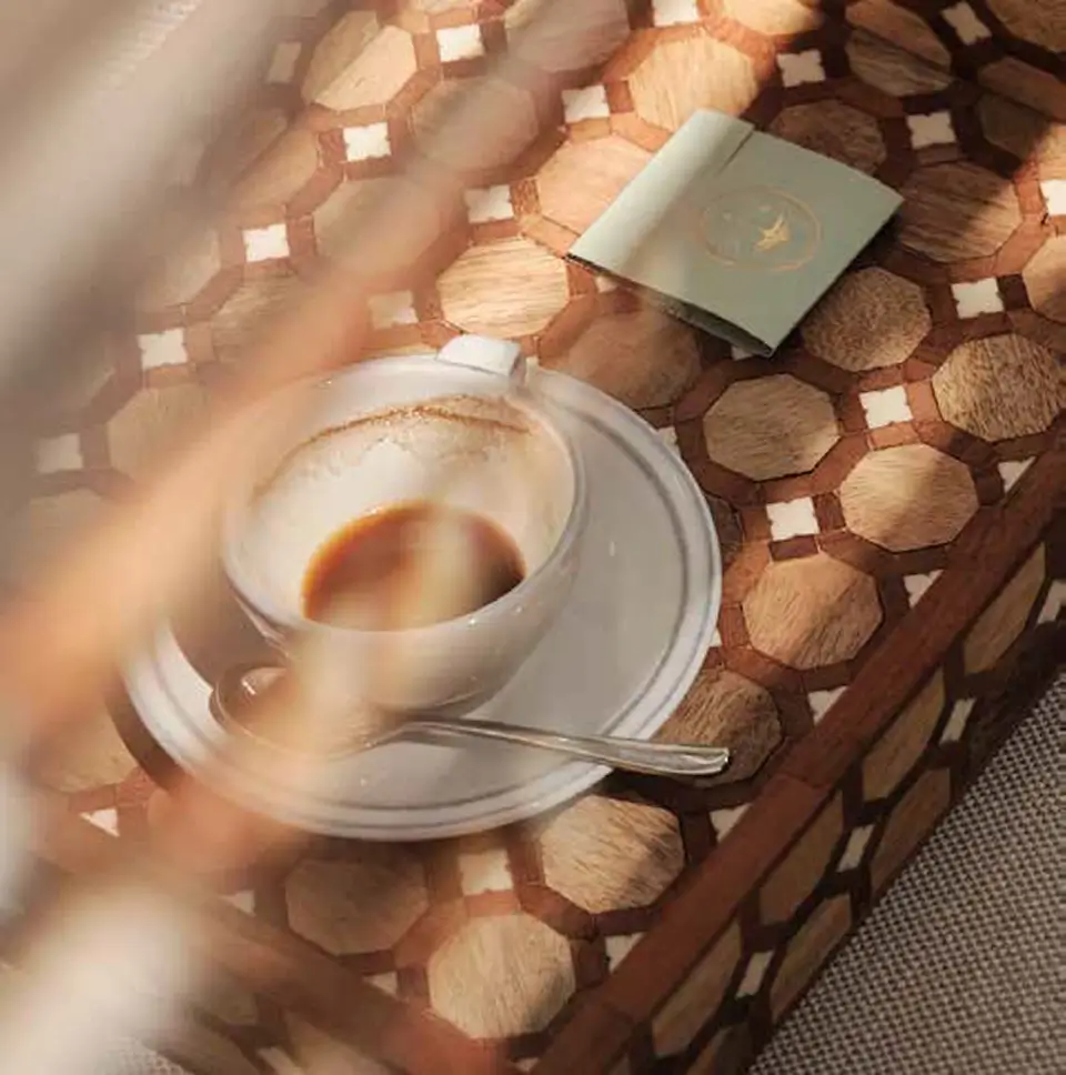 Partially consumed coffee in a white cup on a decorative wooden table beside a green booklet.