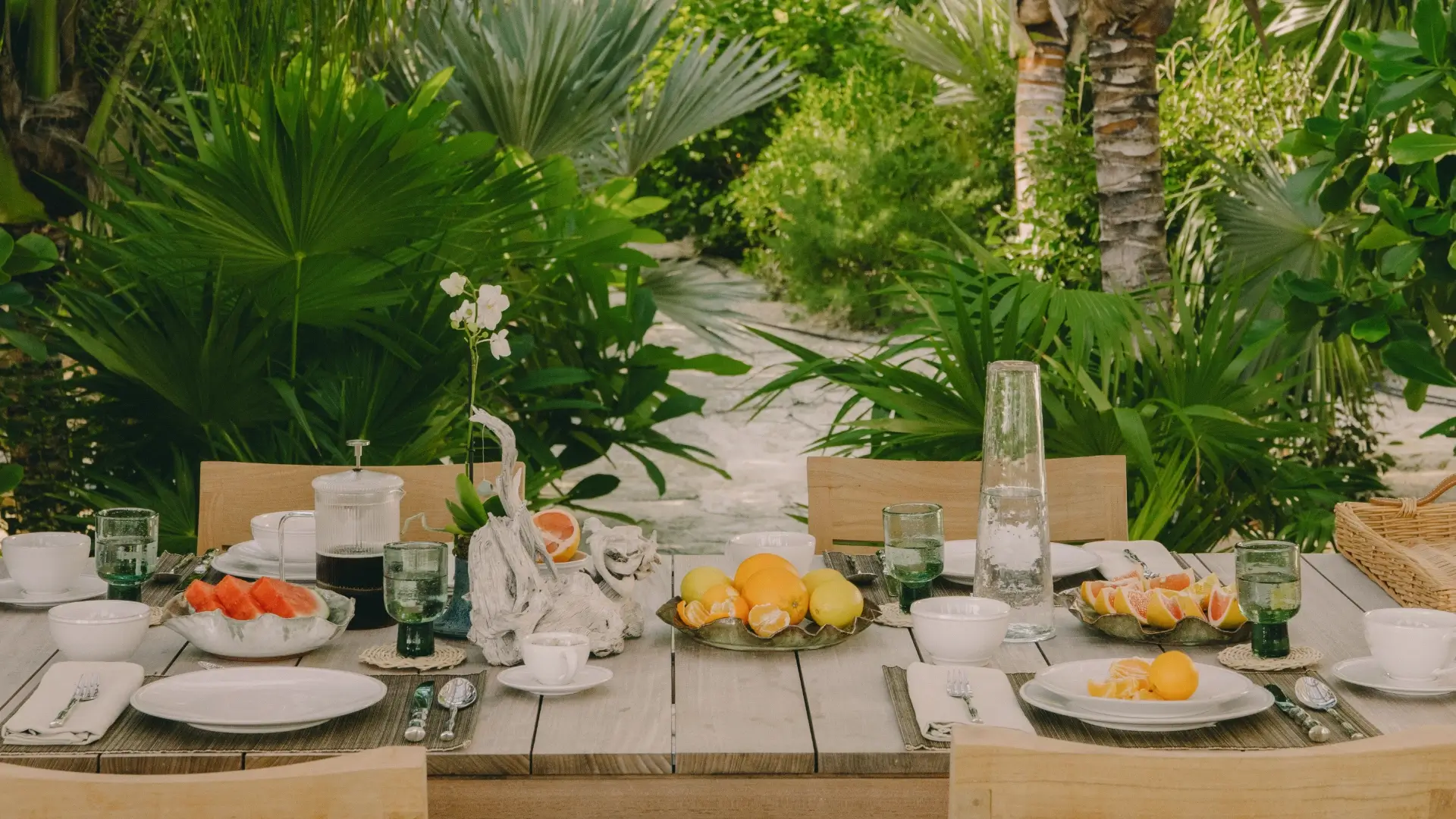 Outdoor dining table set with breakfast, orange juice, croissants, bread, fruit, and ocean view seating.