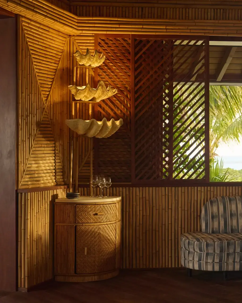 Cozy corner with bamboo walls, a wicker cabinet, three shell-shaped lamps, and a patterned armchair.