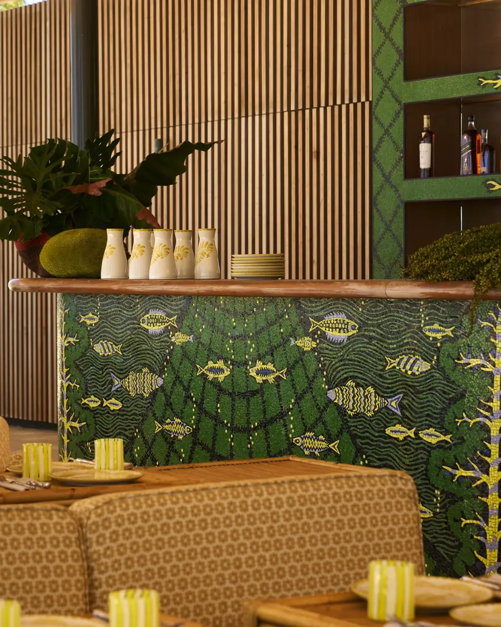 Indoor seating area with decorative counter featuring green mosaic fish and wooden slat wall backdrop.