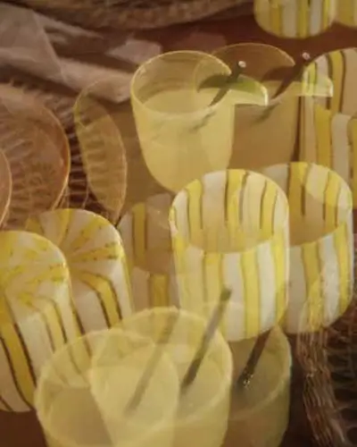 Collection of ceramic cups with yellow and brown vertical stripes placed on woven rattan trays, overlapping due to double exposure effect.