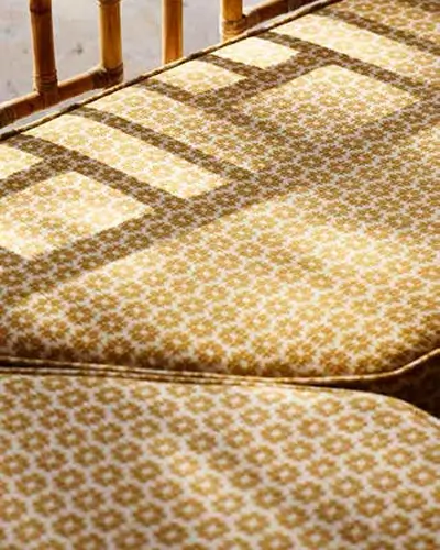 Close-up of a patterned cushioned bench seat with shadows of wooden chair backs cast on it in warm sunlight.