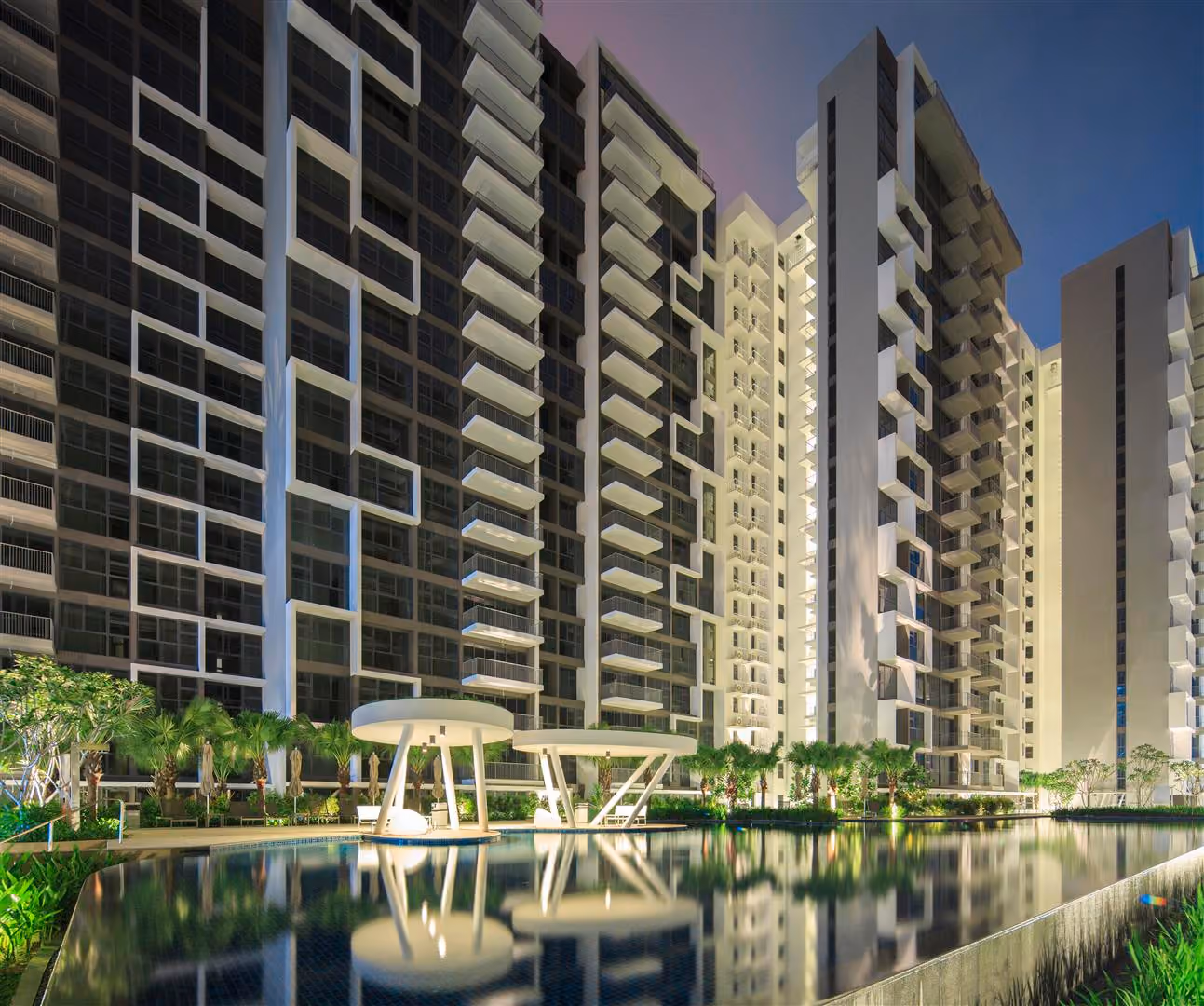 View of Blossom residences with balconies reflected in a calm pool during twilight with landscape lighting.