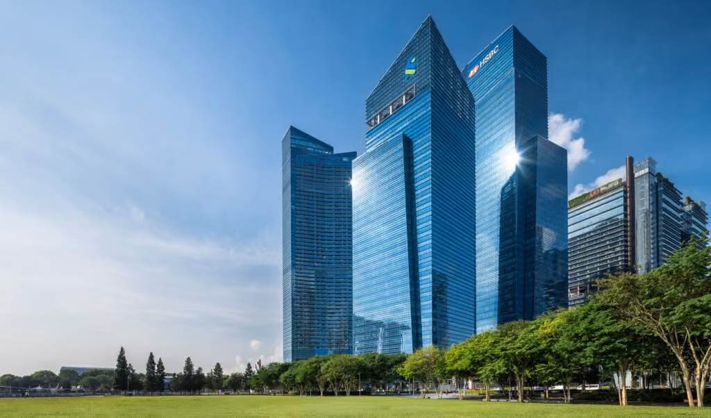 Outdoor view of the MBFC tower showing a cluster of modern glass skyscrapers reflecting sunlight beside green lawn and trees.