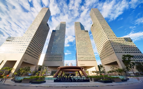 View of Suntec towers showing four tall modern skyscrapers with unique shapes under a partly cloudy blue sky.