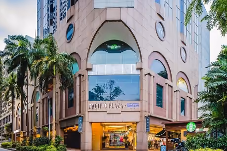 Corner view of Pacific Plaza building with round windows, palm trees, and a Starbucks entrance.