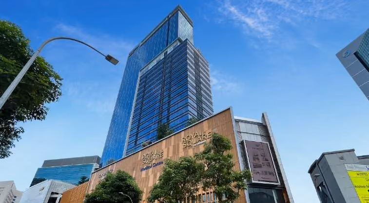 Tall modern glass skyscraper above a building labeled Royal Square against a blue sky.