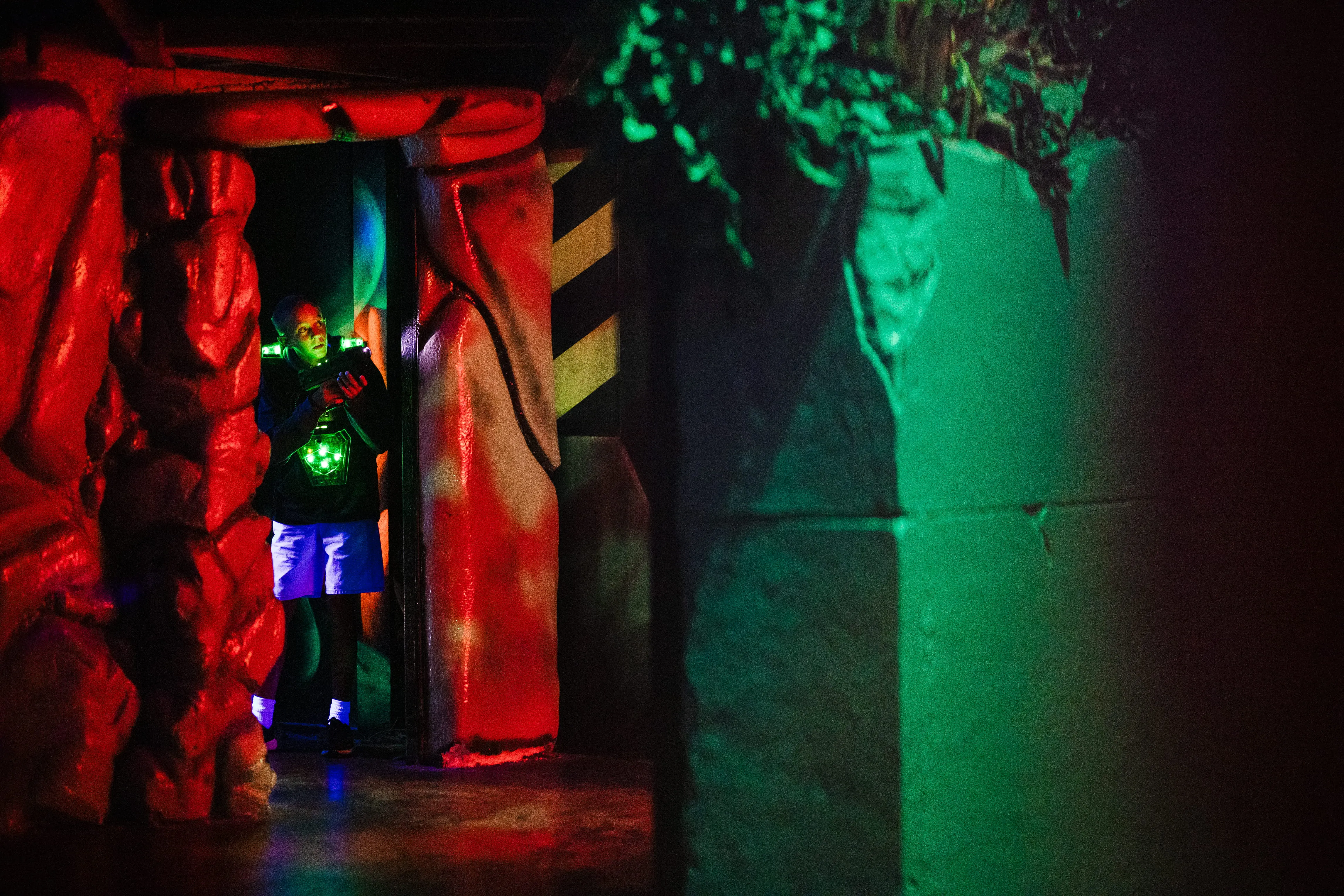 Joueur de laser game dans un couloir de roche éclairé en rouge et vert