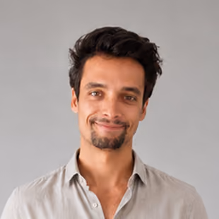 Smiling man with short dark hair and light shirt against plain gray background.