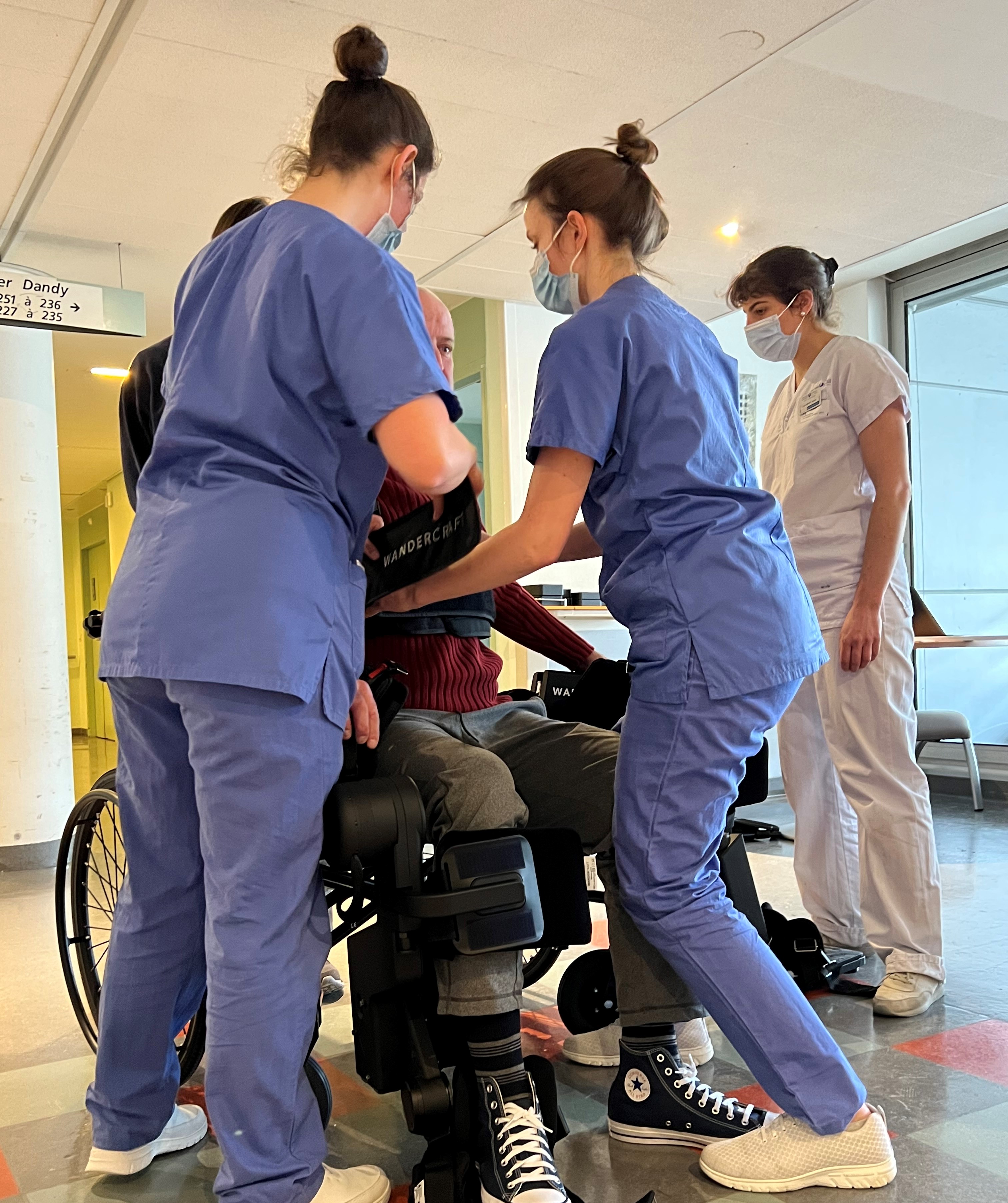 Two nurses supporting a patient standing up in the Atalante X exoskeleton on a hospital ward