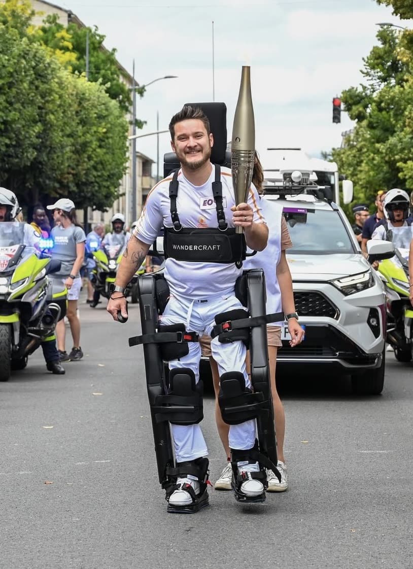 A Wandercraft pilot walking in an Atalante exoskeleton while carrying the Paris 2024 torch