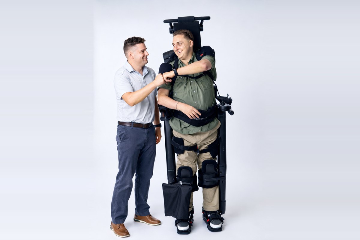 Weston standing in the Eve personal exoskeleton, fist-bumping a clinician in a studio