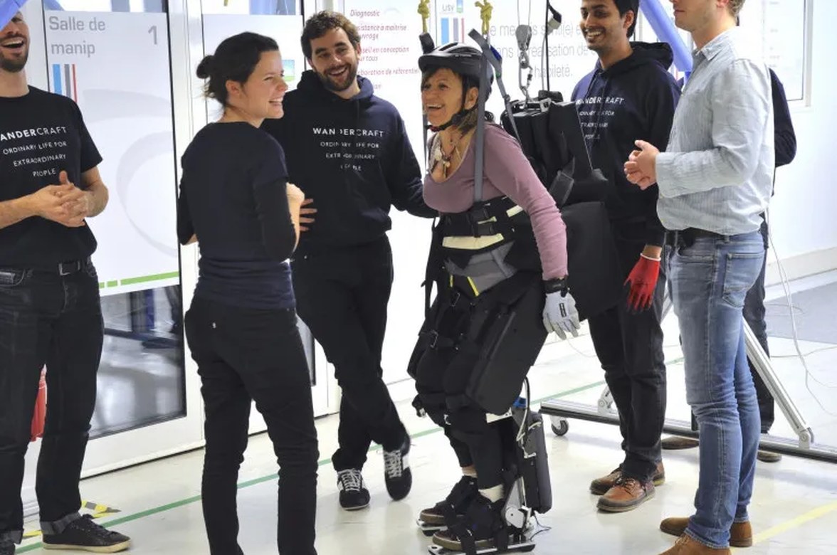 A user walking in a Wandercraft exoskeleton in the test laboratory, surrounded by the engineering team