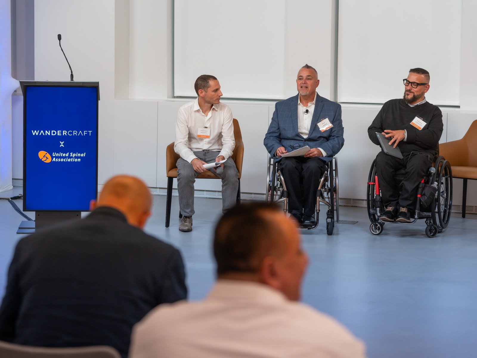 Three panelists on stage at a Wandercraft and United Spinal Association event, two of them in wheelchairs