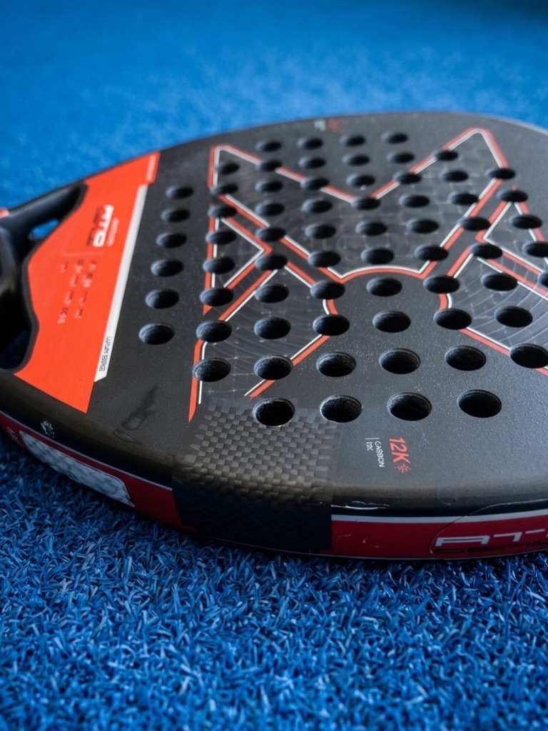 Close-up van een rood-zwart padelracket met 12K carbon blad en geometrisch patroon