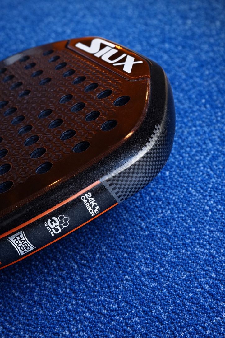 Close-up van een Siux padelracket met oranje-zwart 24K Carbon Hard Touch-blad
