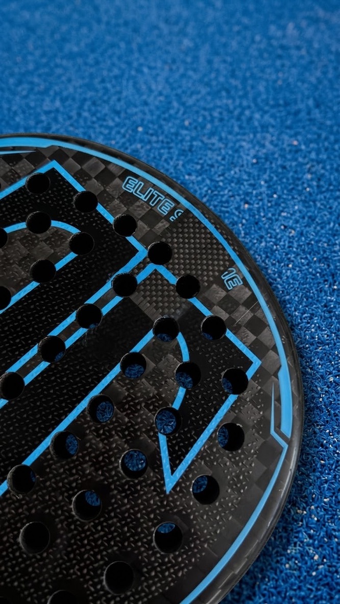 Close-up van een zwart-blauw padelracket met Elite-opdruk op de padelbaan