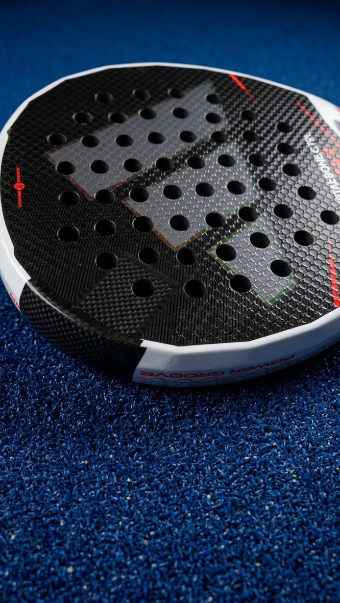 Close-up van een zwart-wit padelracket met Power Groove-opdruk op de padelbaan