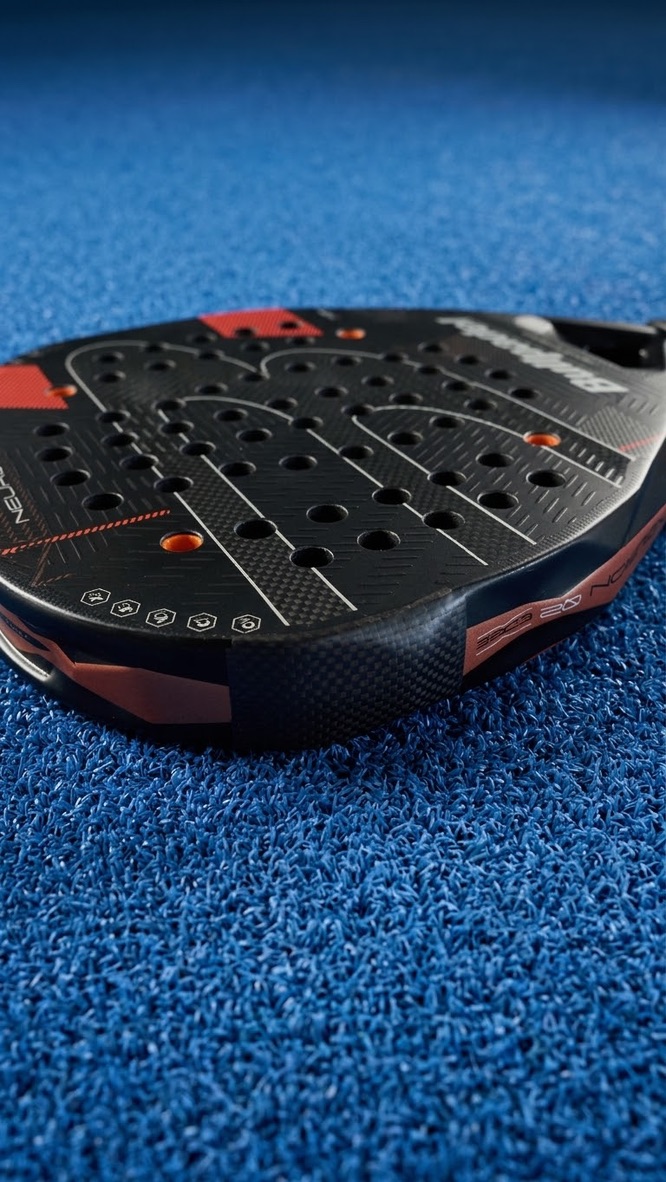 Close-up van een zwart-rood padelracket met driehoekig patroon op de padelbaan