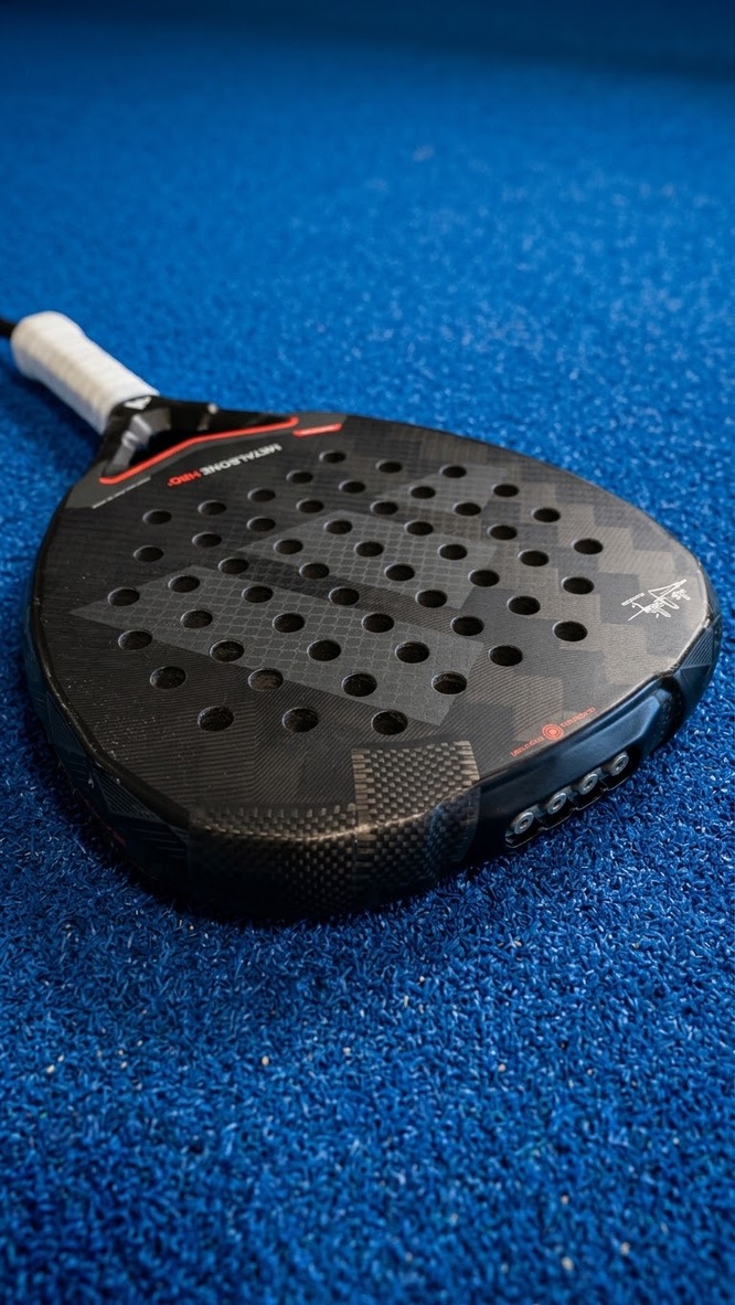 Close-up van een zwart padelracket met rode accentlijnen op de padelbaan