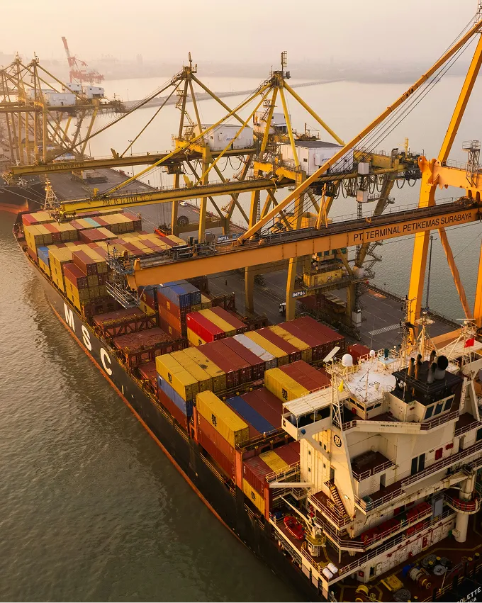 A large container ship docked at terminal cranes loading and unloading colorful shipping containers.