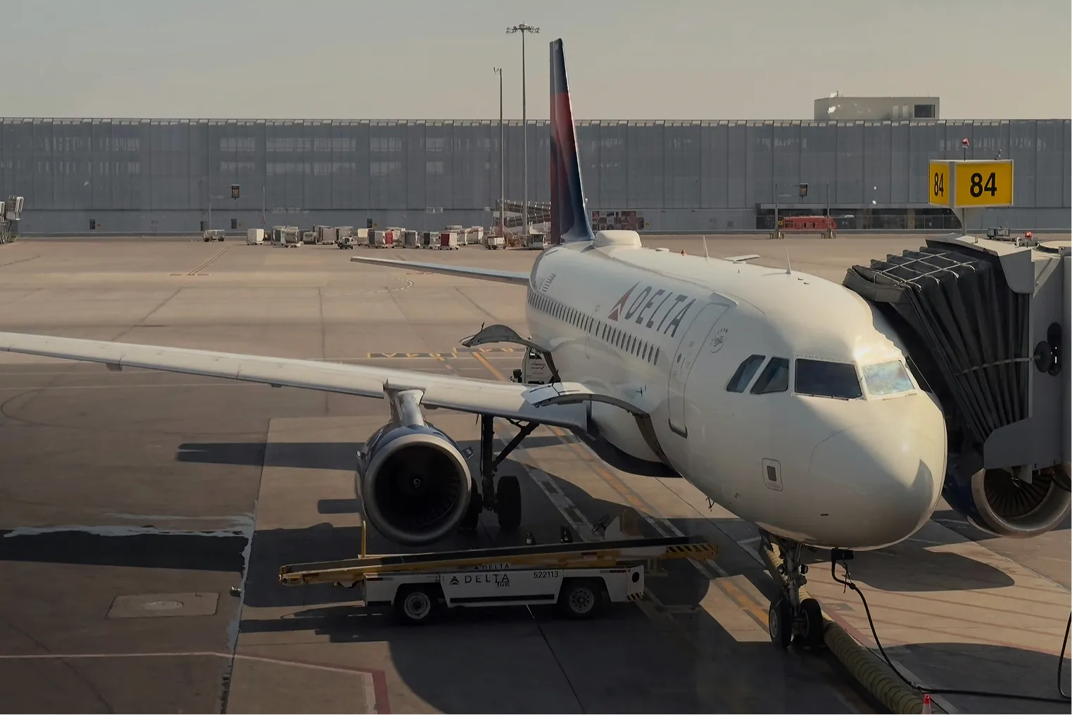 Delta Airlines plane parked at gate 84 connected to jet bridge at an airport.