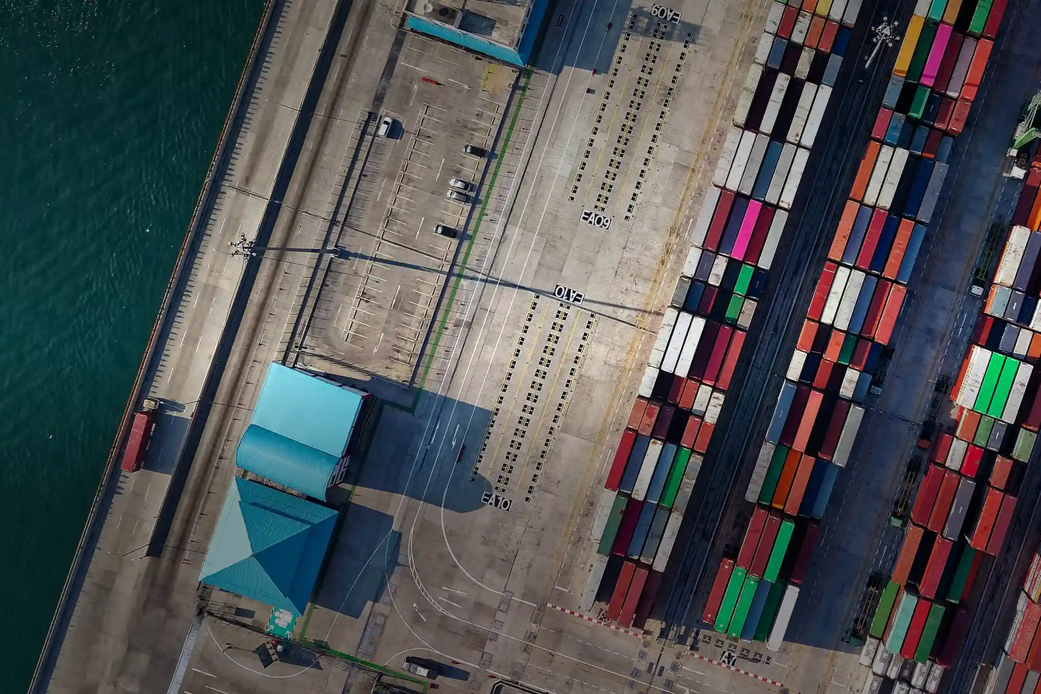 Aerial view of a shipping port with colorful containers, dockside buildings, and water.