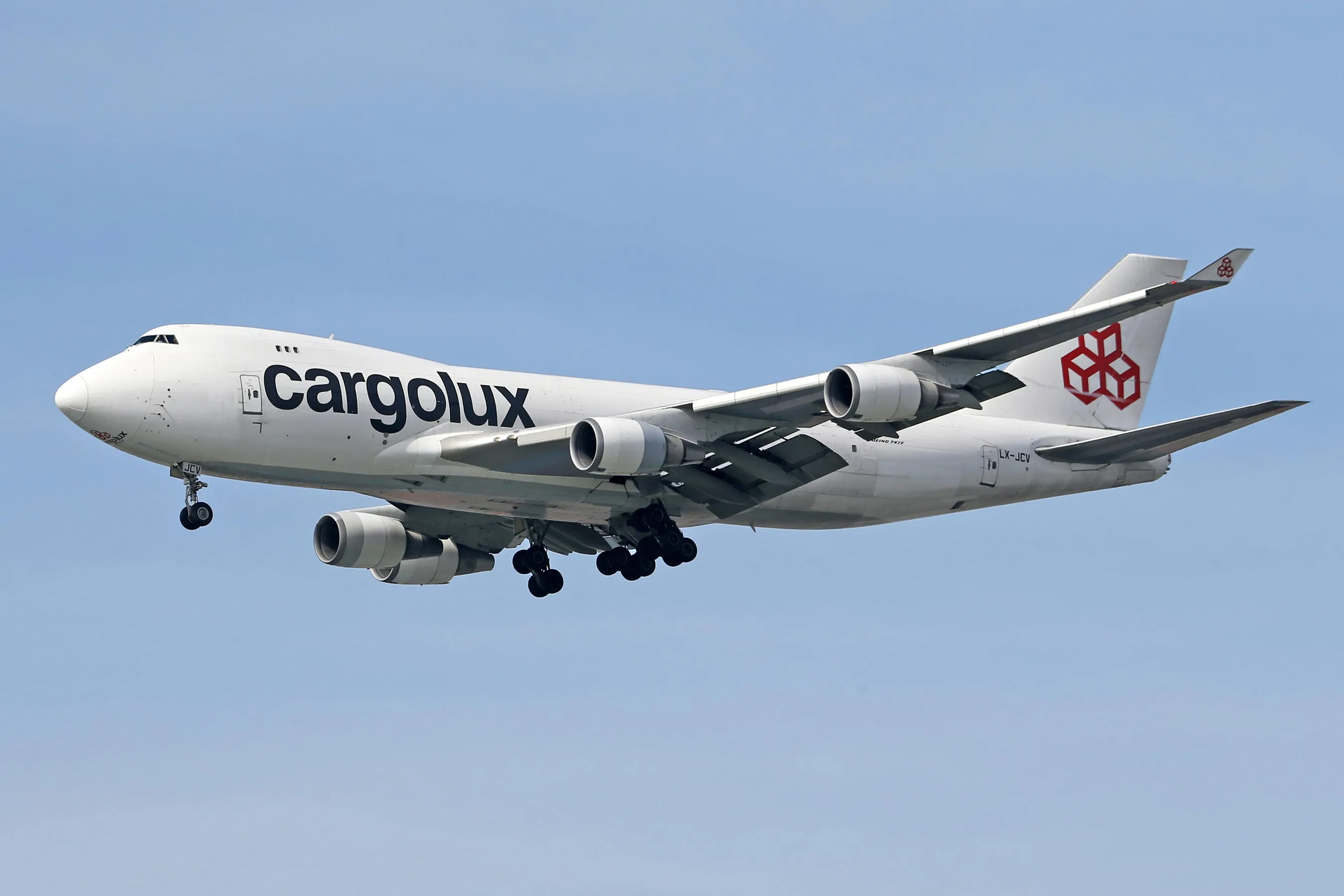 Cargolux cargo airplane with landing gears down flying against a clear blue sky.
