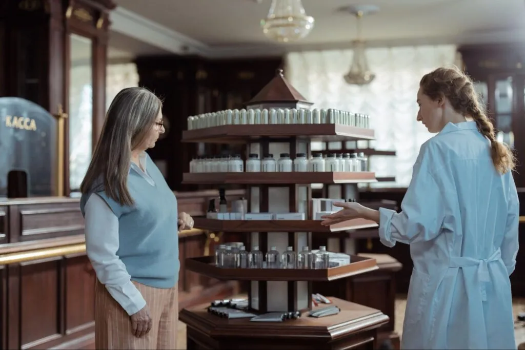 A pharmacist and a customer are looking at items on a shelf together.