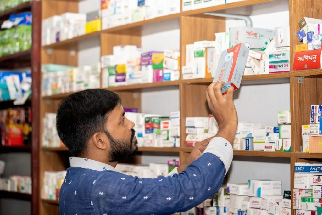 A person is grabbing a rectangular medicine box from a wooden shelf, which is stocked with various medications.