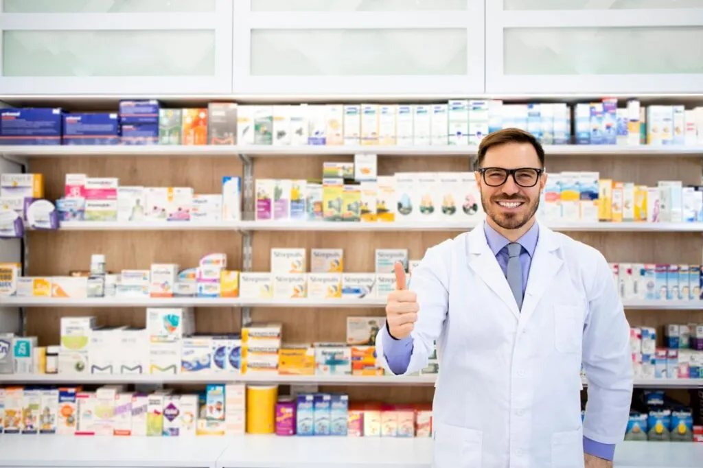 Portrait of smiling caucasian pharmacist standing in drug store with thumbs up.