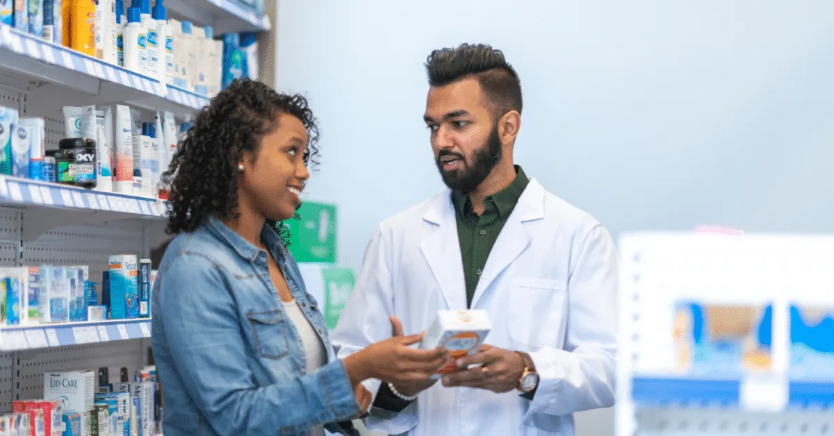 Pharmacist assisting a customer with a product in the pharmacy aisle, representing patient support and medication guidance.