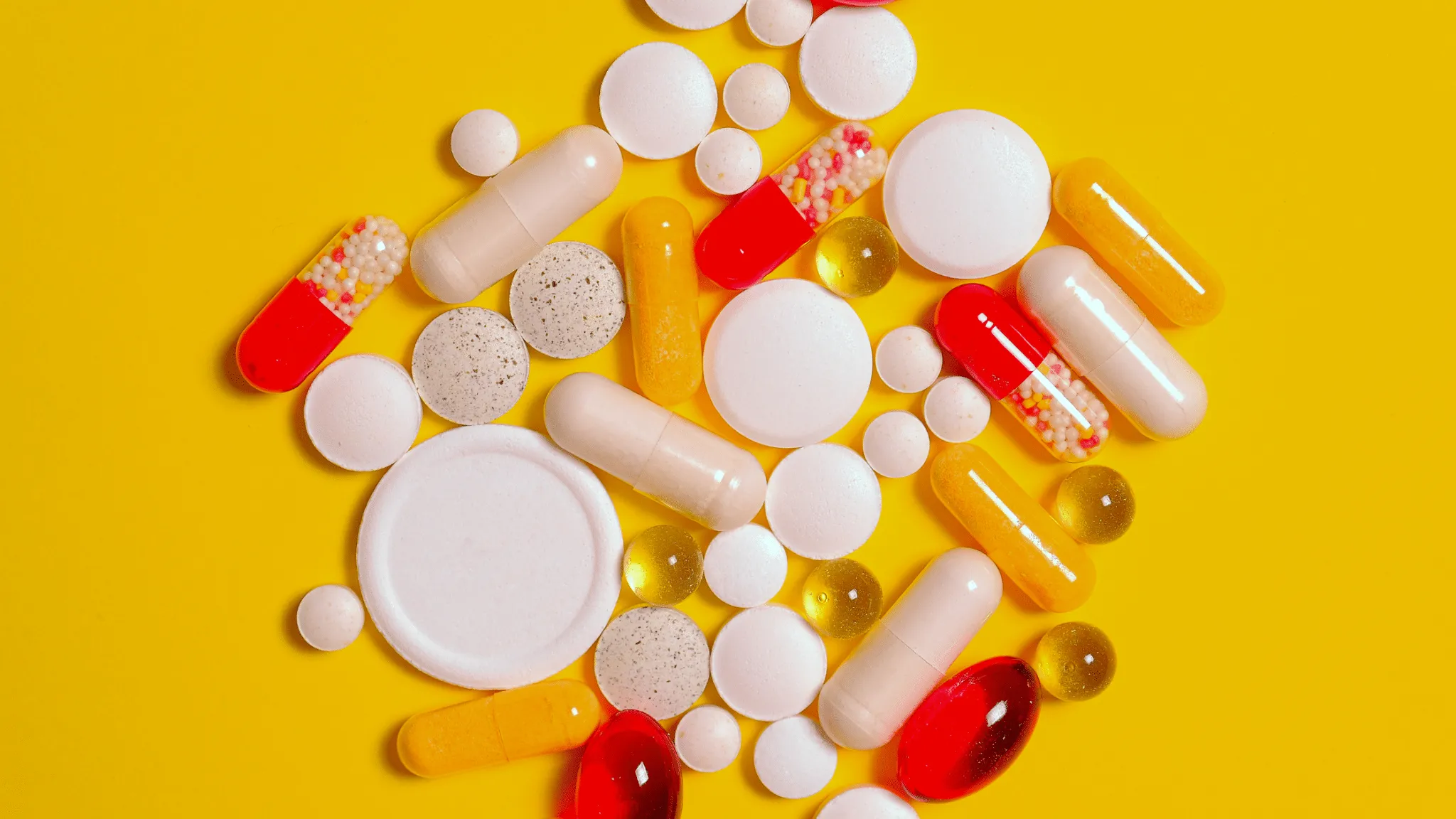 White, yellow, and red pills and capsules laying against a yellow background.