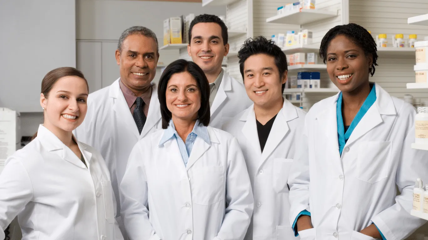 A group of six pharmacists standing together smiling in a pharmacy.