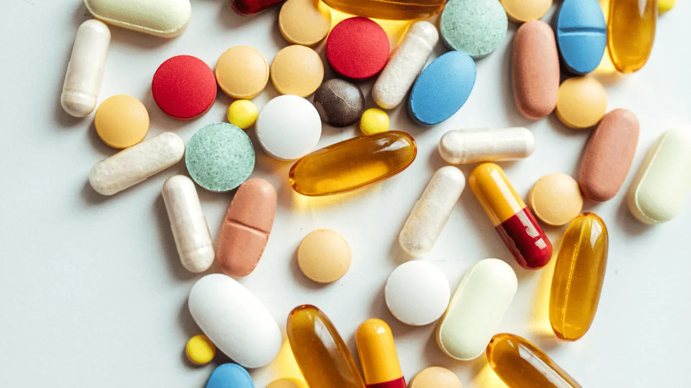Assorted colorful pills and capsules are scattered on a white surface.