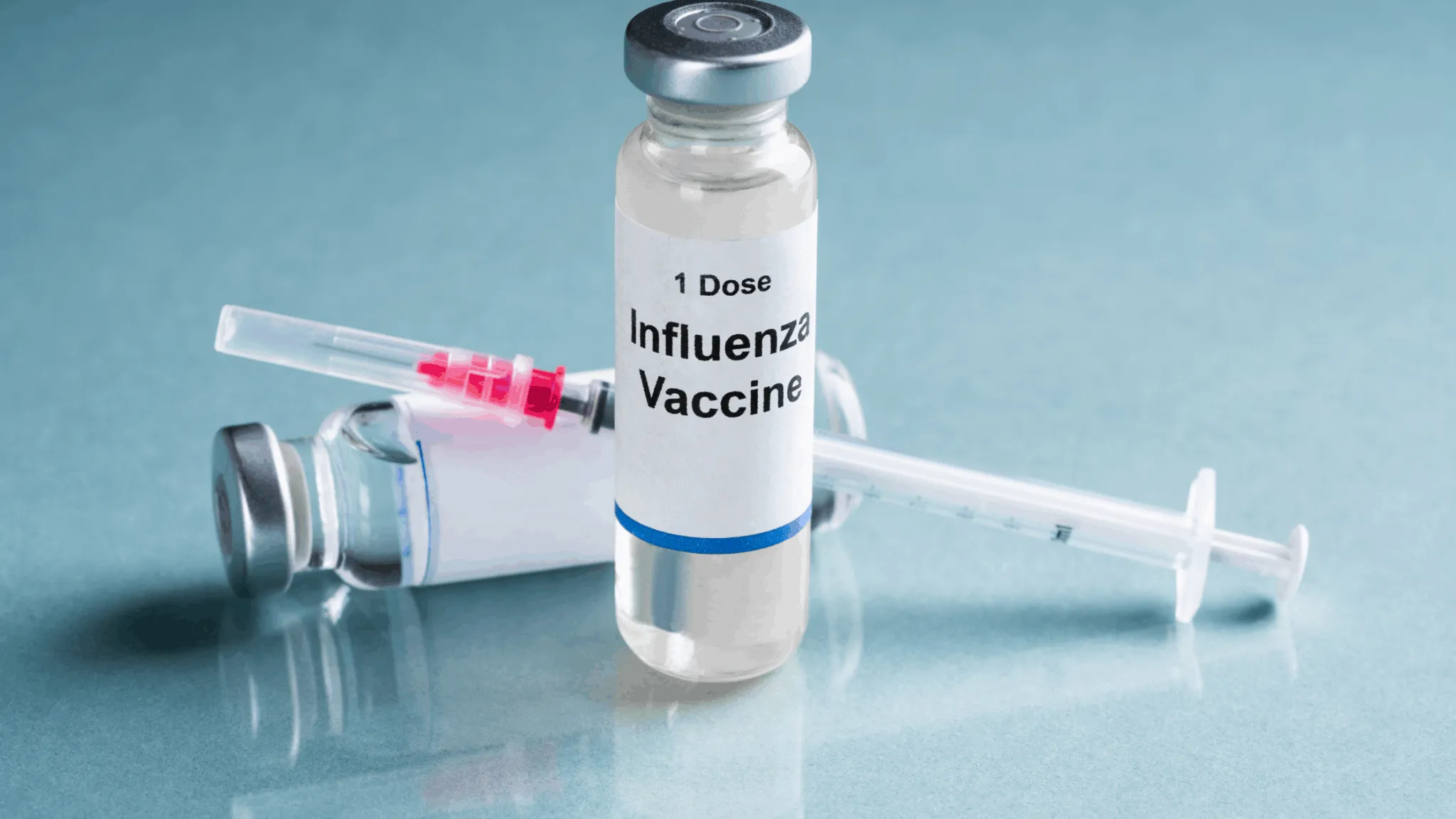 Influenza vaccine vial and syringe on a medical surface.
