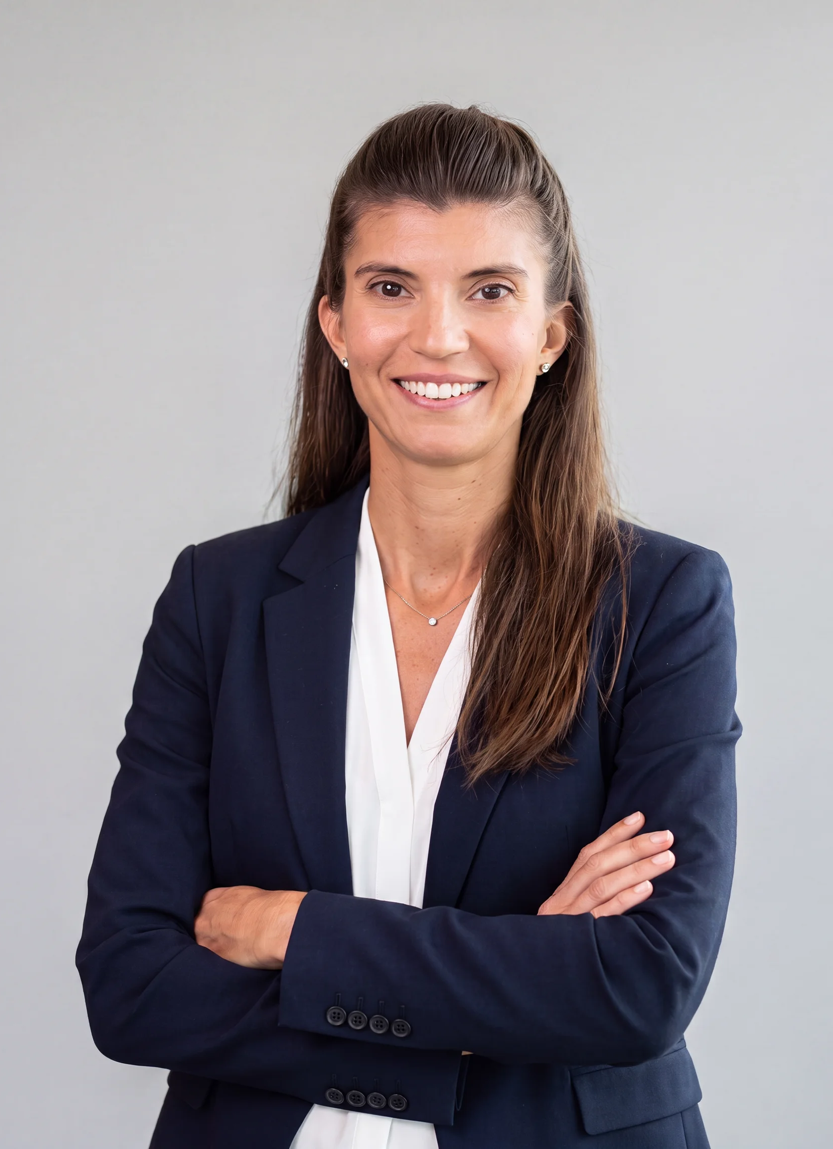Confident young woman in a light gray business suit standing indoors with hands in pockets and smiling.