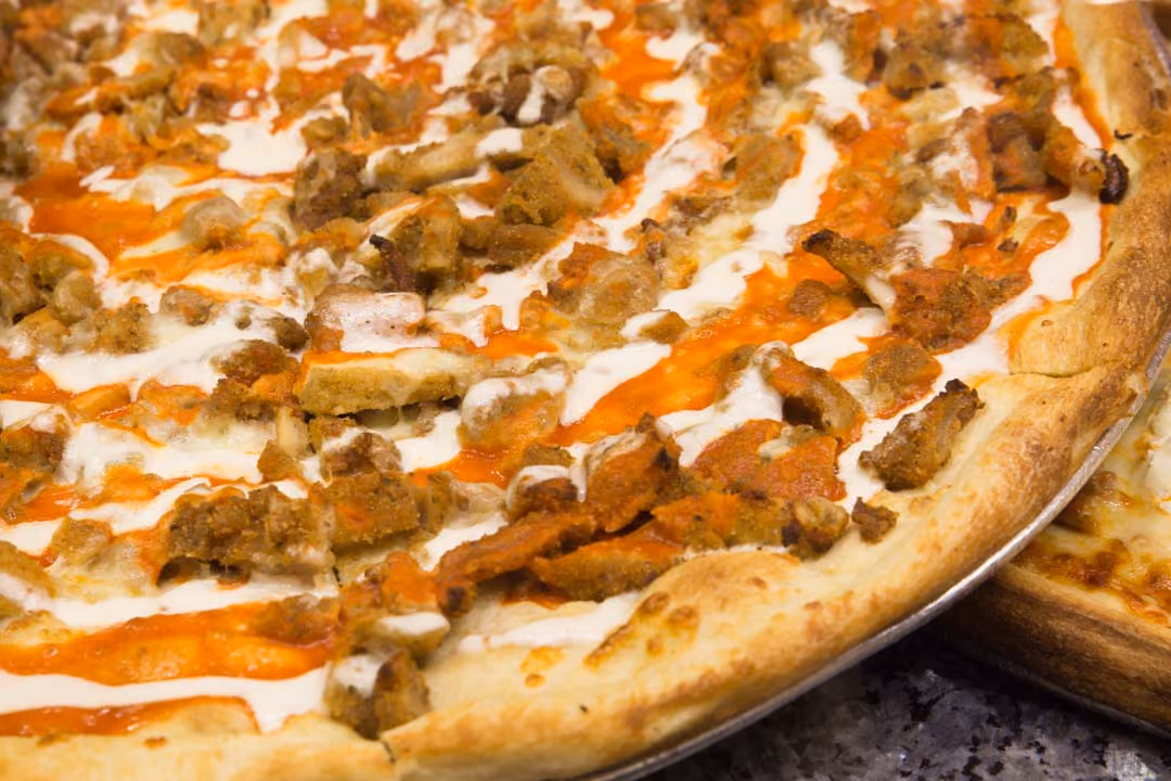 Buffalo wing pizza topped with buffalo sauce, ranch drizzle, and chunks of chicken on a golden crust.