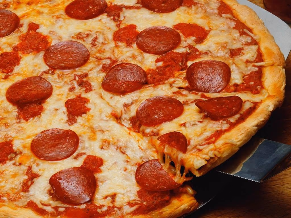 Pepperoni pizza with melted cheese and one slice being lifted with cheese stretching.
