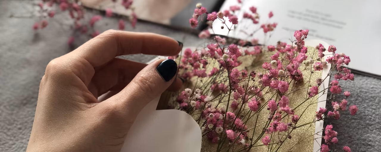 A delicate hand holds a white envelope with pink flowers inside, adding an artistic touch.
