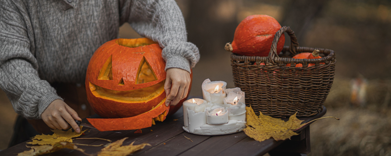 Woman carving a pumpkin outdoors with candles and autumn leaves.