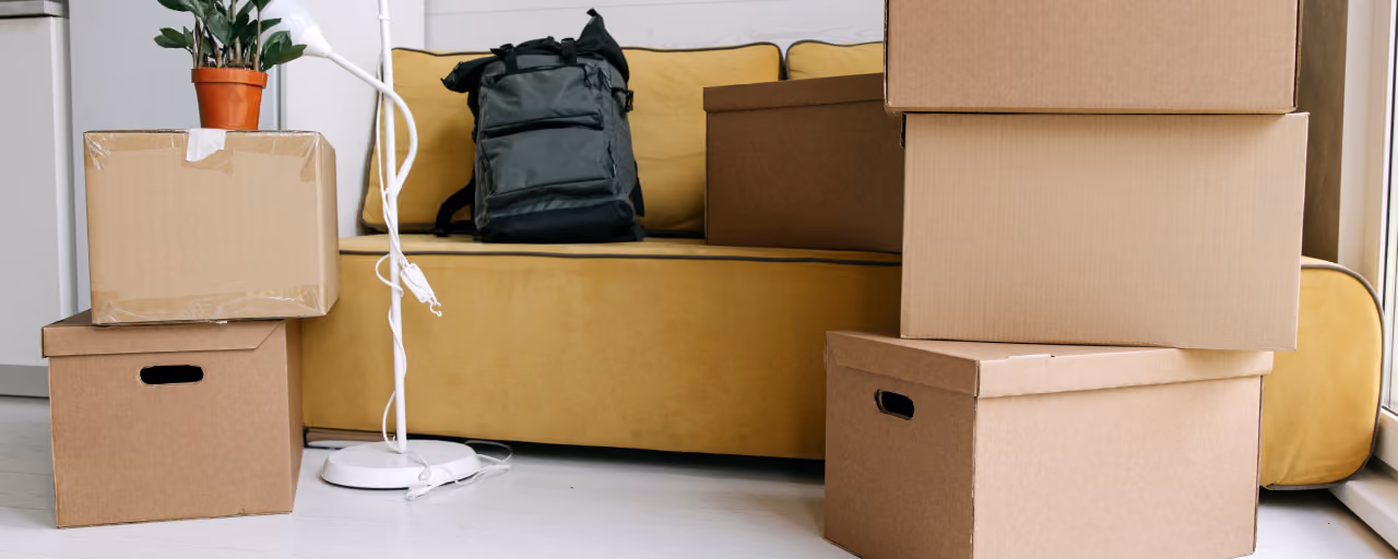 Cardboard boxes and a backpack in a cozy living room signify moving day excitement.