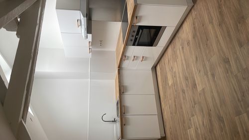 Minimalist white kitchen with wooden countertops, built-in oven, sink, and wood floor under angled ceiling beams.